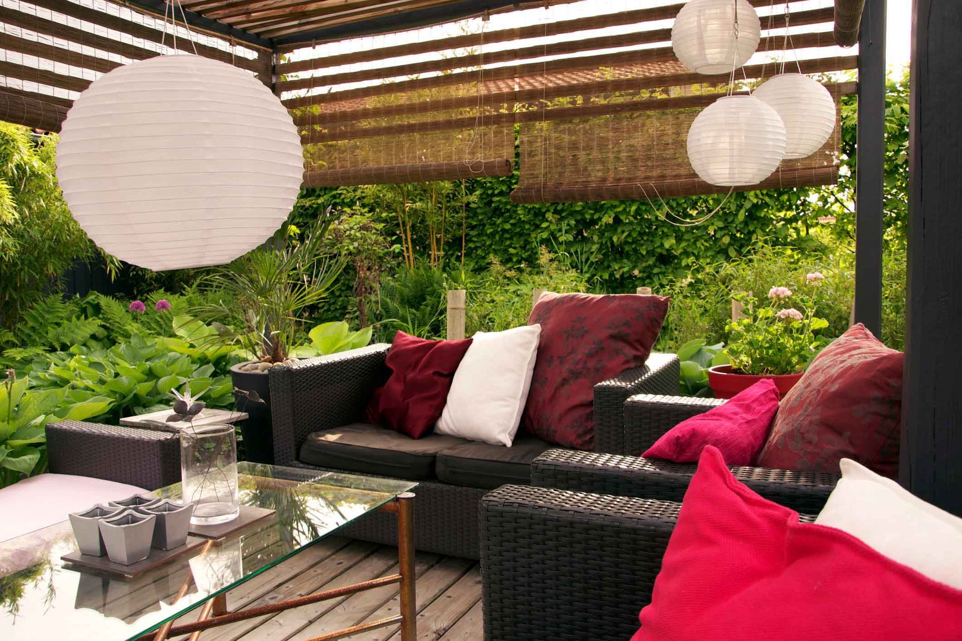 Outdoor seating area with sofa, pillows, hanging paper lanterns, and lush greenery.