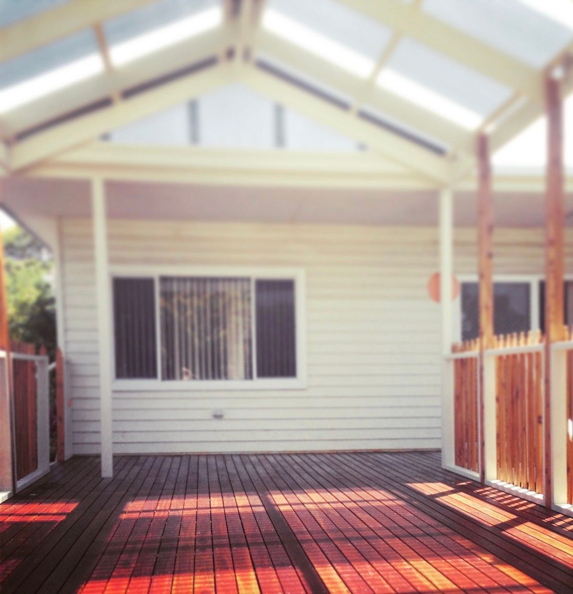 Wooden deck with a covered patio in front of a white house.