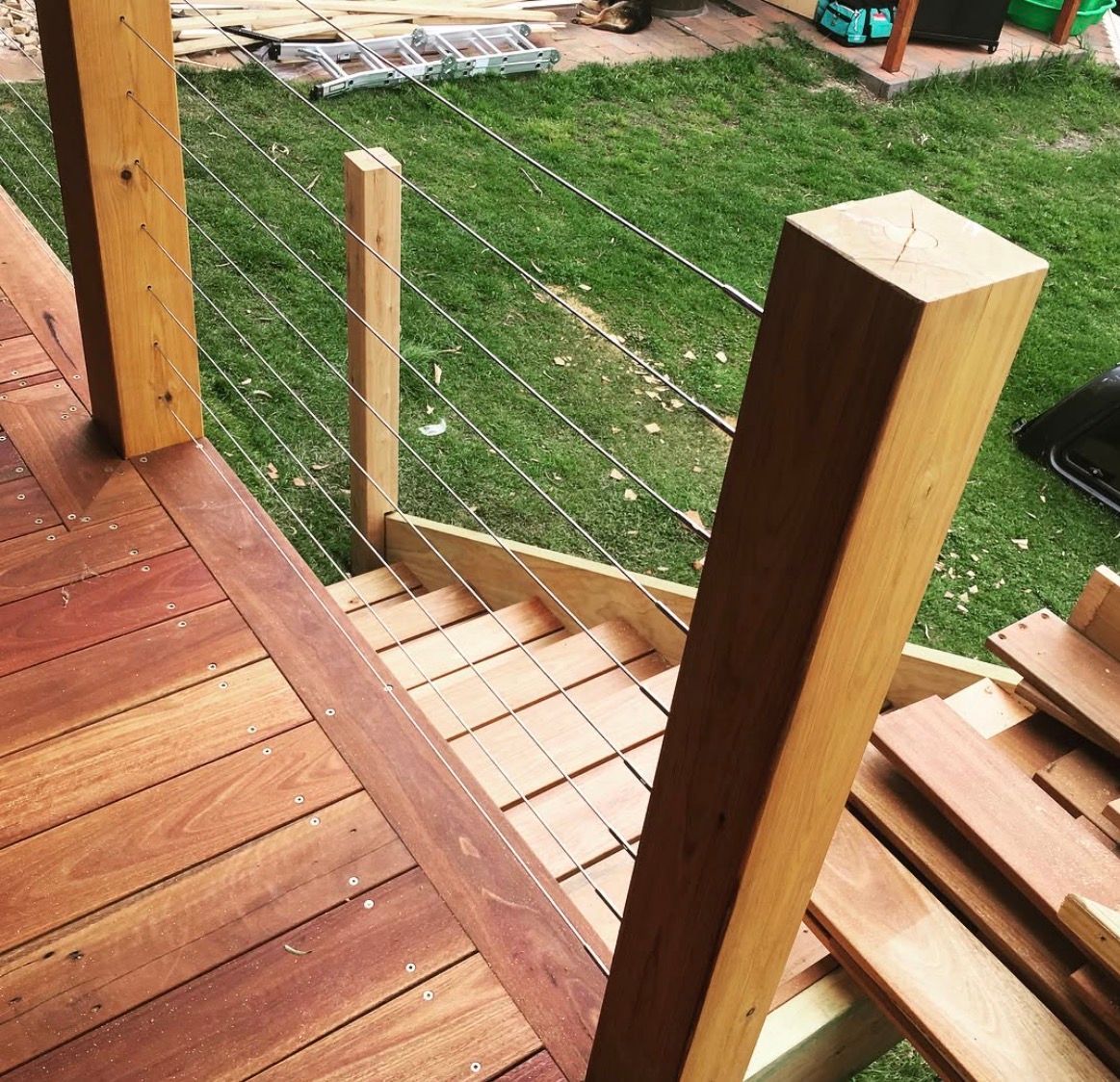 Wooden deck with cable railings and steps. Green grass in the background.
