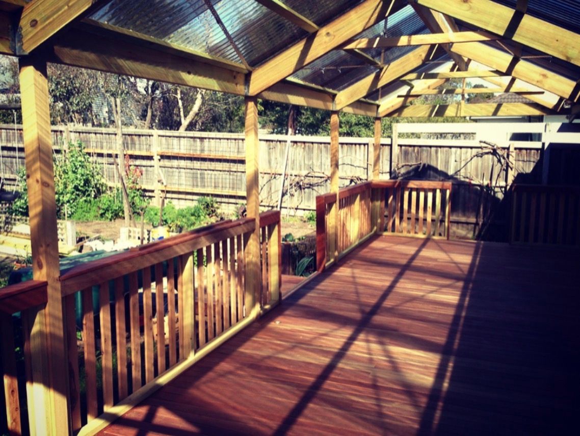 Wooden deck with ramp and covered roof, overlooking a backyard with a fence.