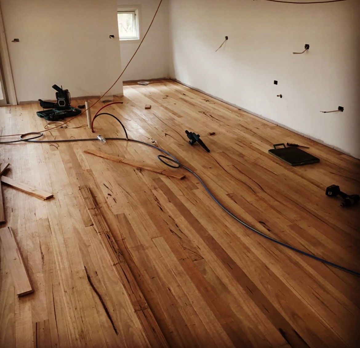 Newly installed hardwood floor in a room under construction, with tools and wiring present.