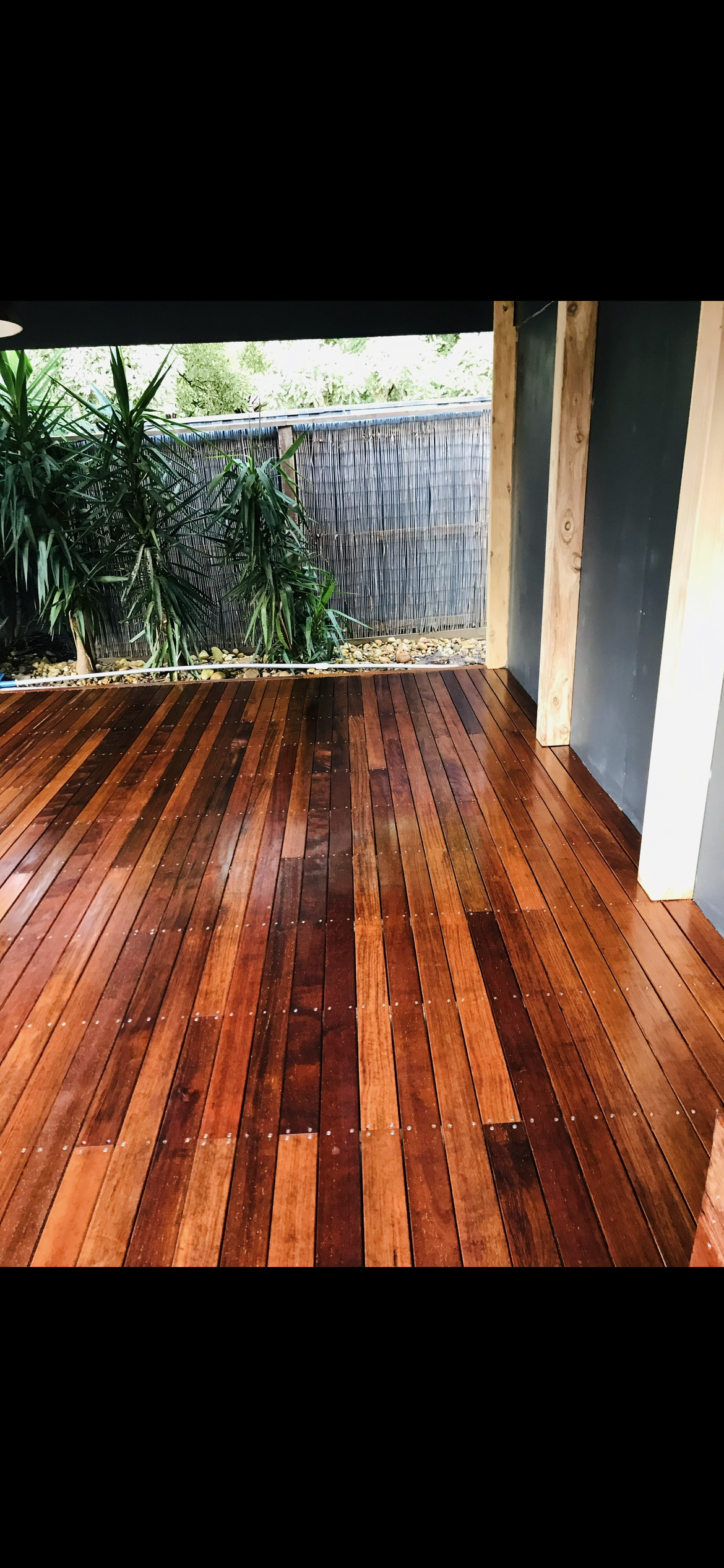 Wooden floor outdoors with greenery and stone wall visible.