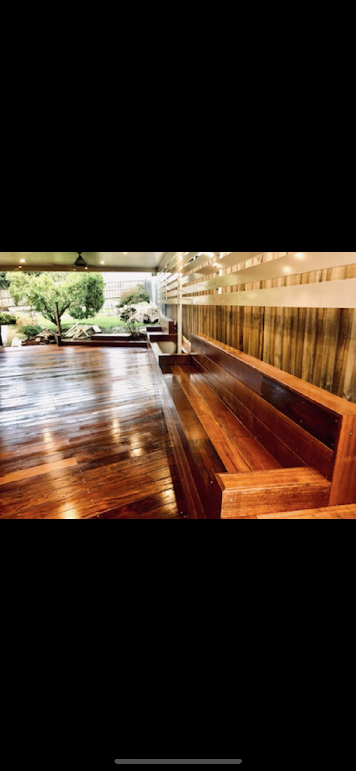 Wooden bench and floor in an outdoor space, with view of trees and greenery.