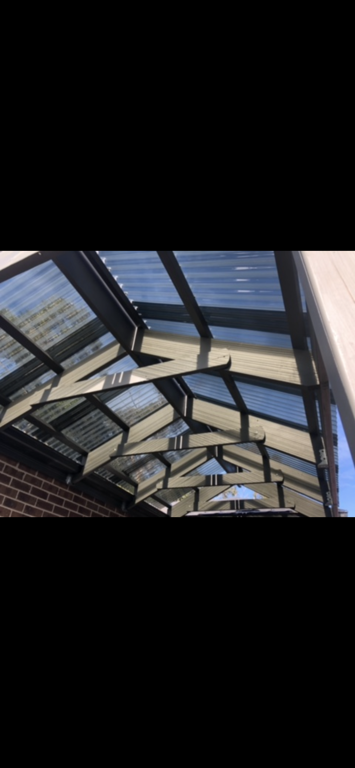 A sloped wooden roof with clear corrugated panels. It is over a brick wall and outdoor area.
