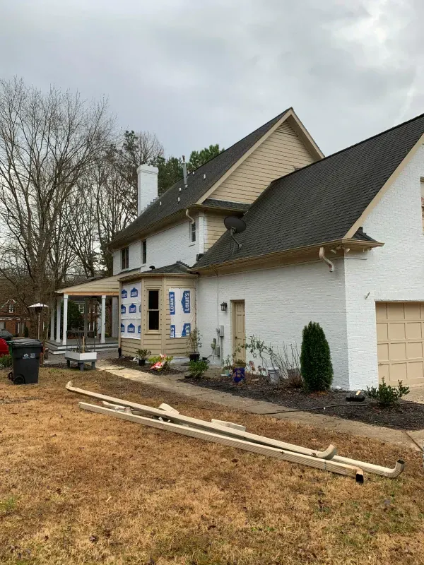 A large white house with a black roof is being remodeled.