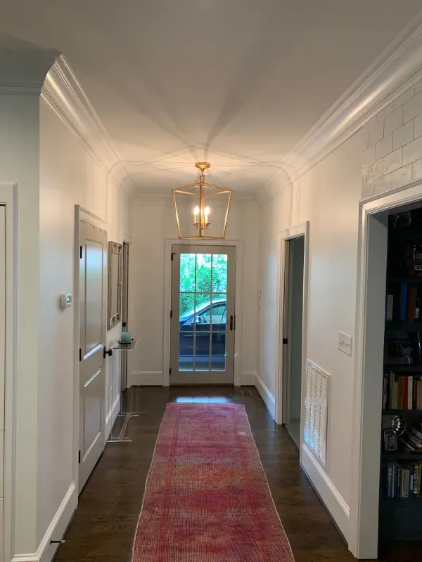 A long hallway with a red rug and a chandelier.
