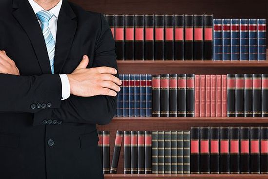 primo piano di avvocato maschio con braccio attraversato in piedi davanti a mensola del libro