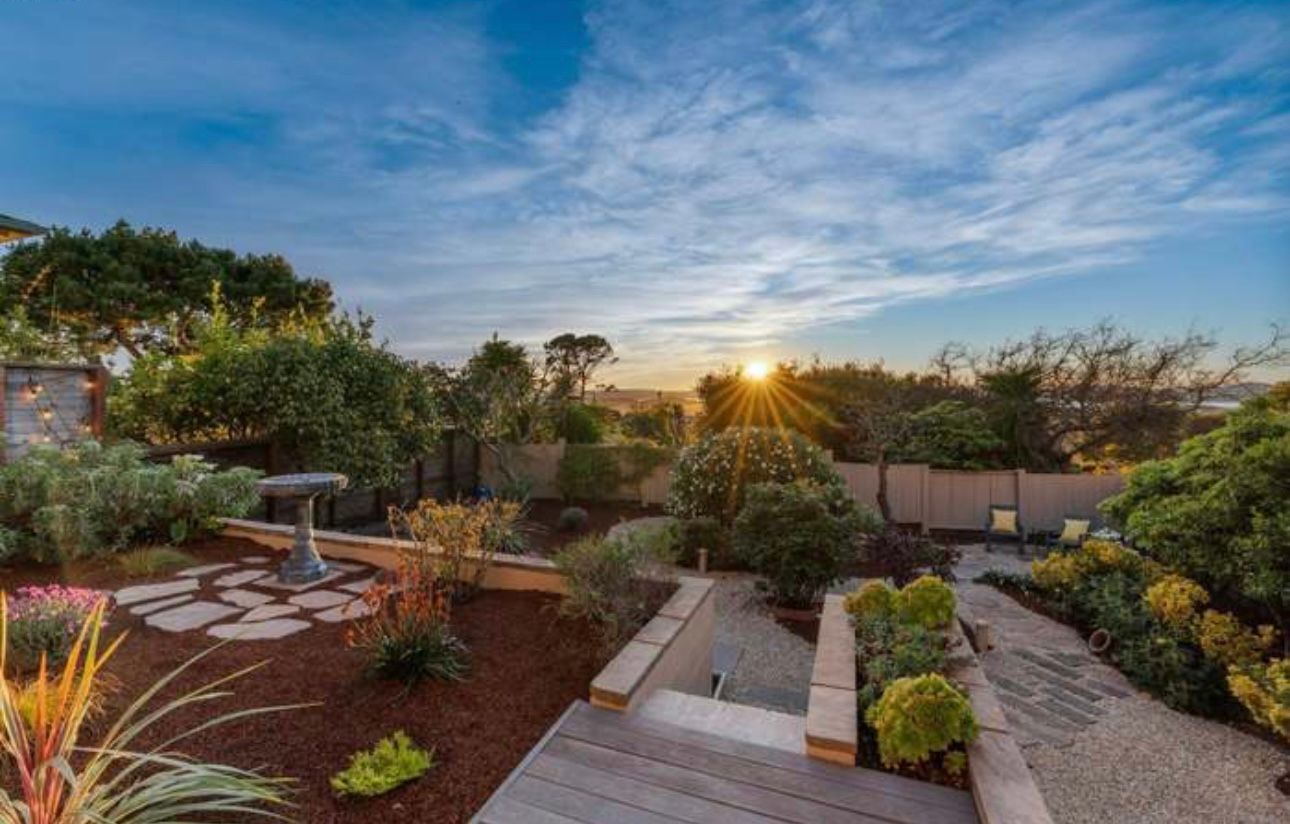 Landscaped backyard with stone steps, shrubs, trees, and a patio seating area
