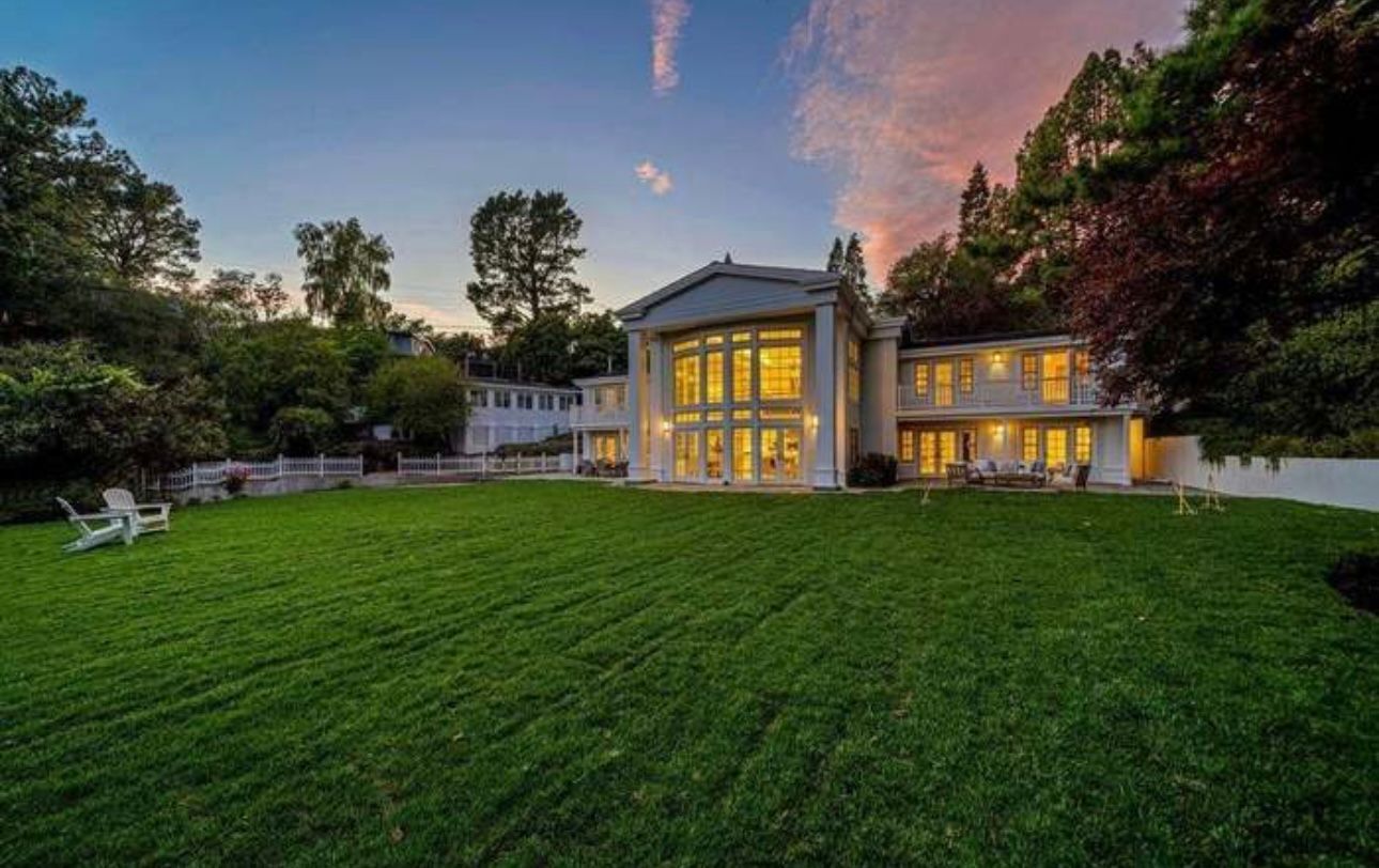 Large modern house with lit windows and a wide green lawn at dusk