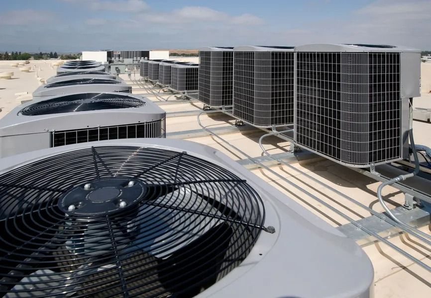 Rooftop view of multiple air conditioning units with large fans, pipes, and metal frames, against a clear sky.