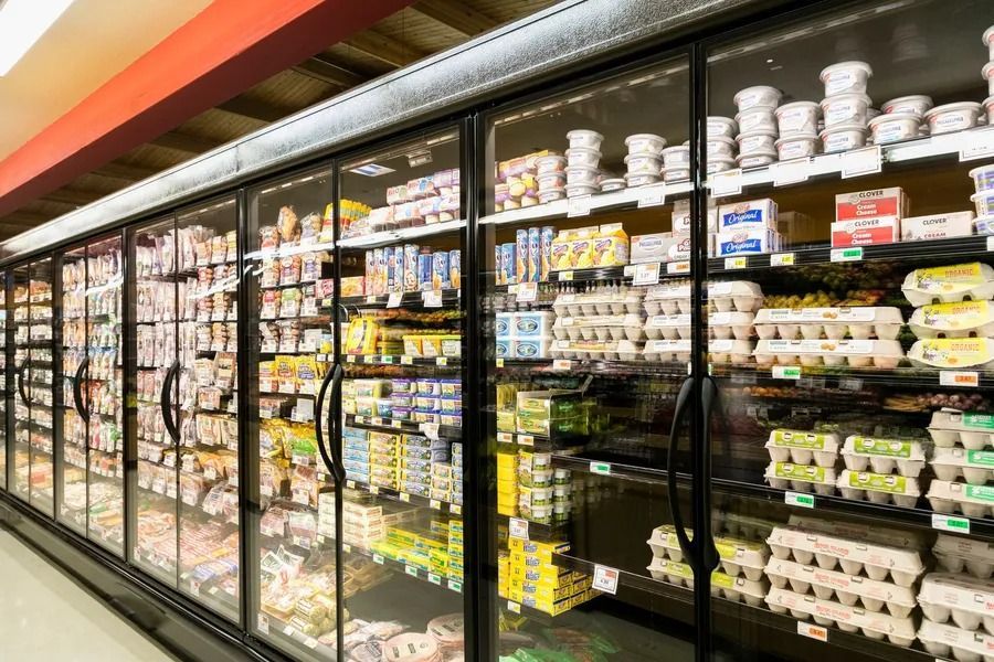 Refrigerated dairy and egg section in a grocery store. Rows of glass-door coolers display various products, including cartons of eggs and containers of yogurt.