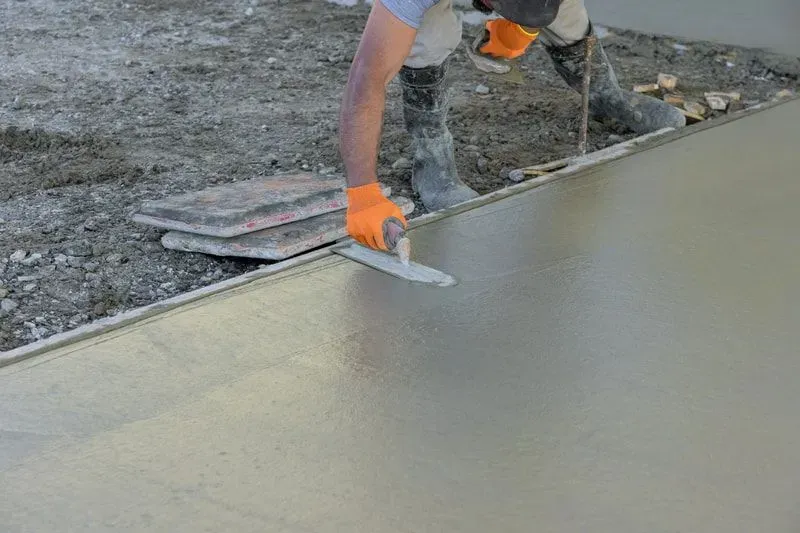 Worker smoothing wet concrete with a trowel on a construction site