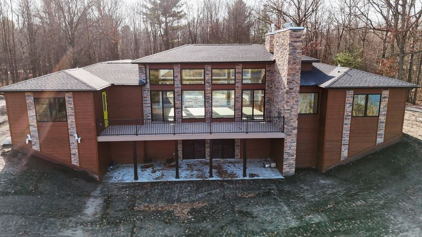 Modern brick house with large windows, central chimney, and a covered patio in a wooded setting