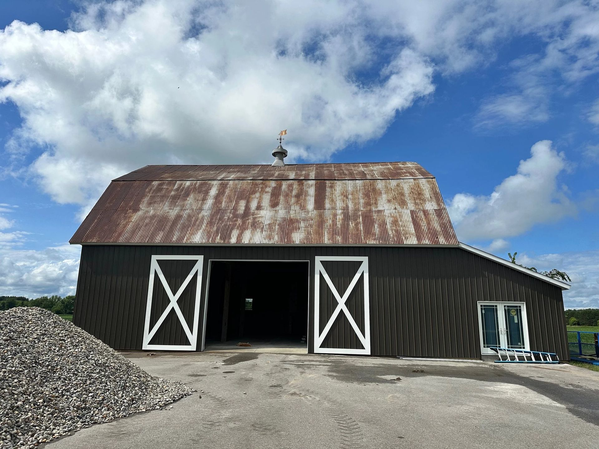 Rustic barn with white doors and a rusted roof under a partly cloudy blue sky