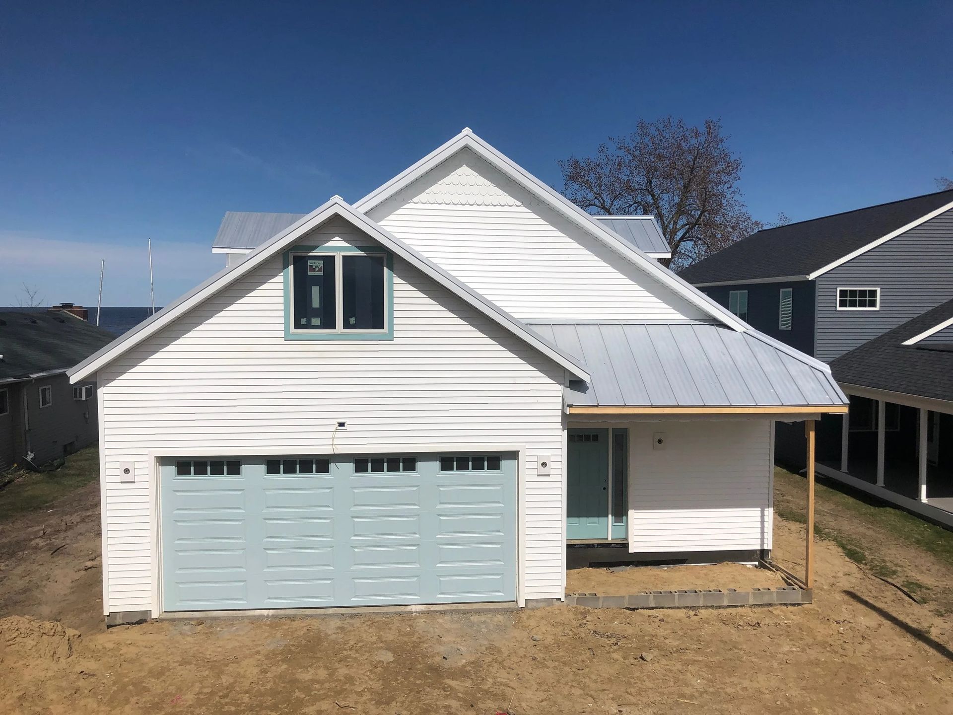 White suburban house with a light blue garage door and dormer windows under a clear blue sky
