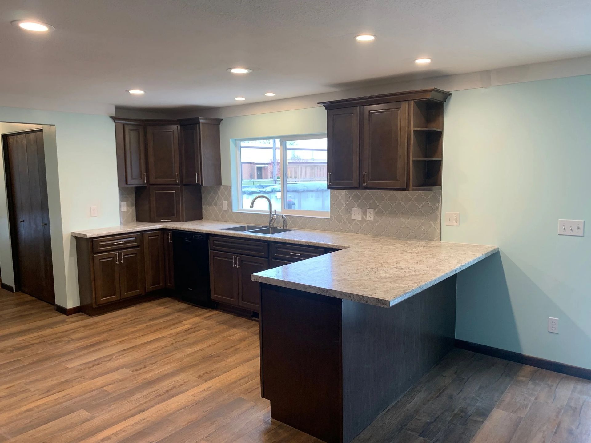 Empty modern kitchen with dark wood cabinets, granite countertops, and a large island in a bright room