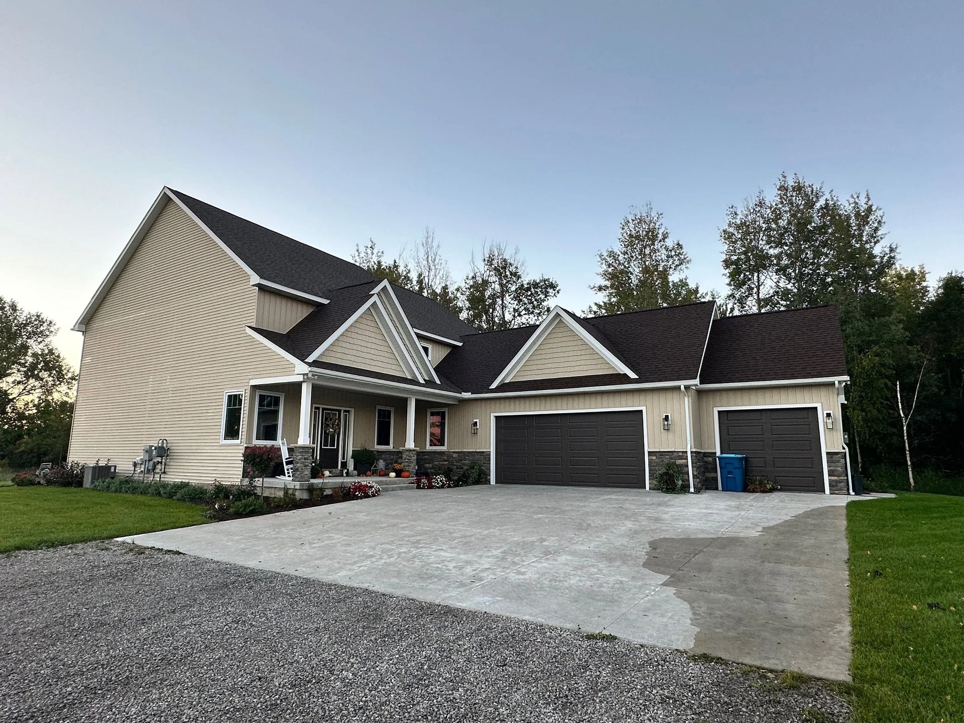 Large beige suburban house with dark roof, two-car garage, and a wide concrete driveway at dusk