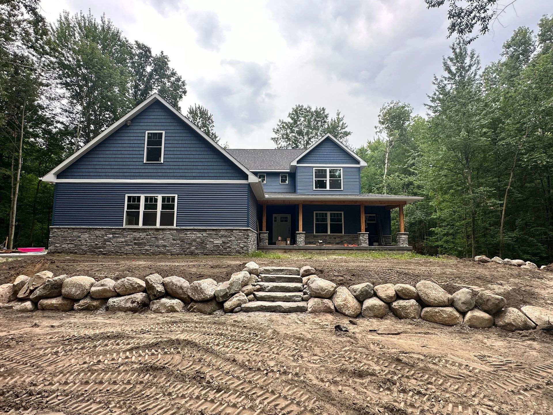 Blue house with stone foundation, front porch, and rock retaining wall in a wooded rural setting
