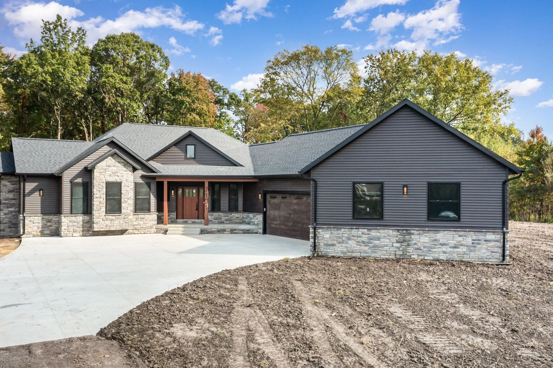 Modern gray house with stone accents, two-car garage, and a wide driveway under a blue sky