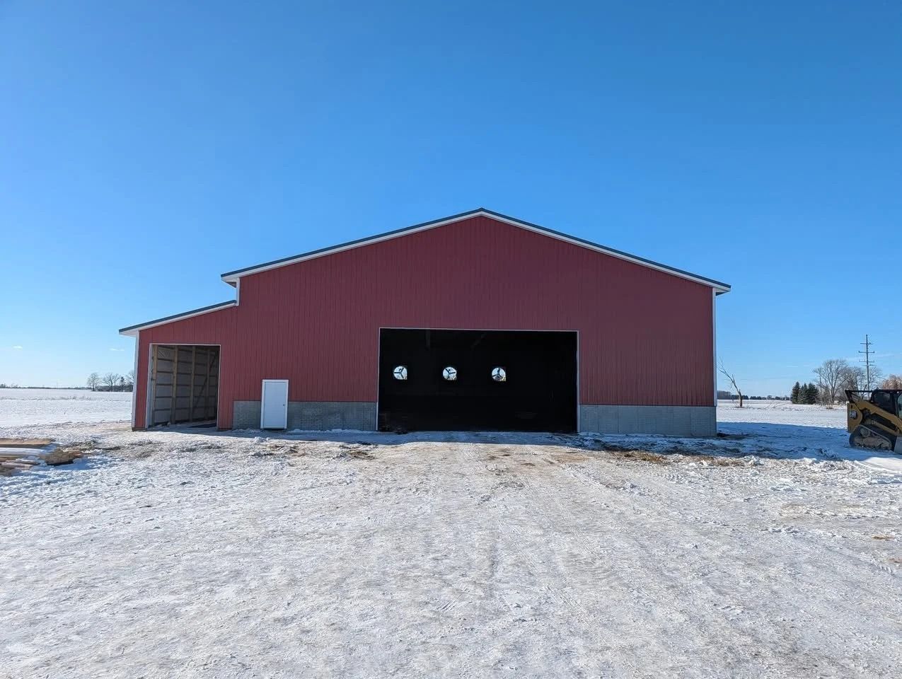 Red barn with open doors on a snowy rural lot under a clear blue sky