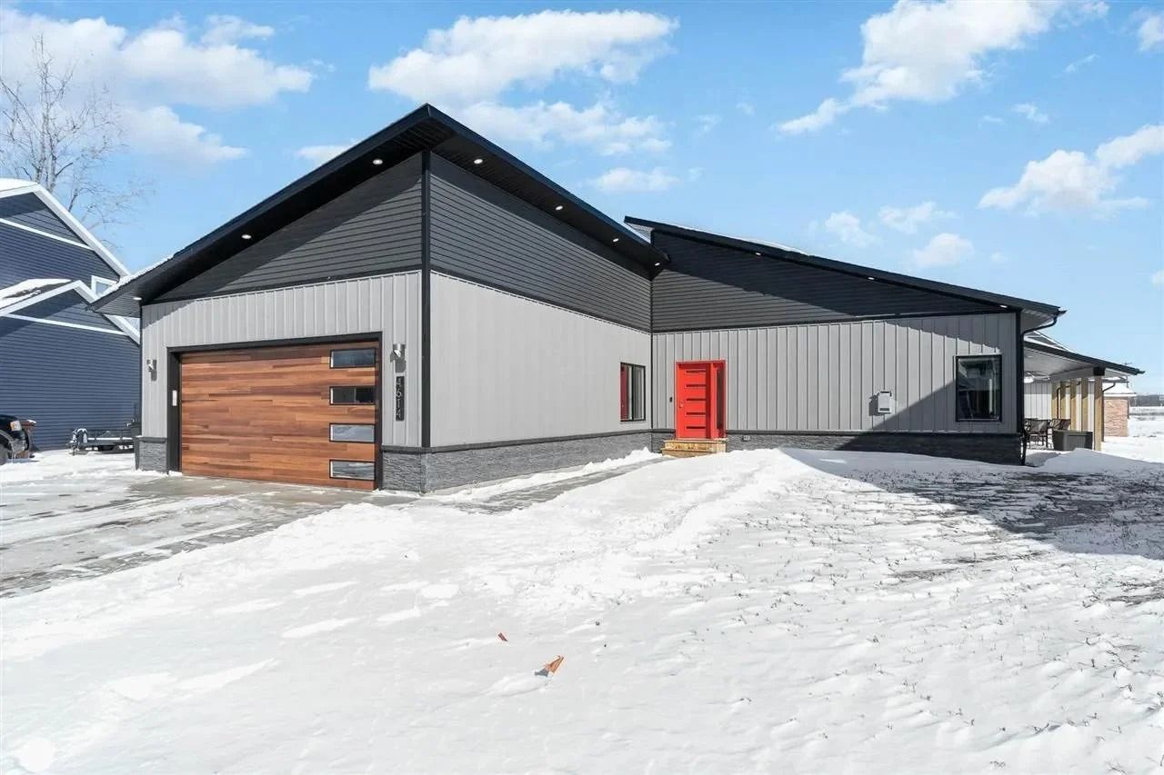 Modern gray industrial building with a wood garage door and red entrance in a snowy landscape