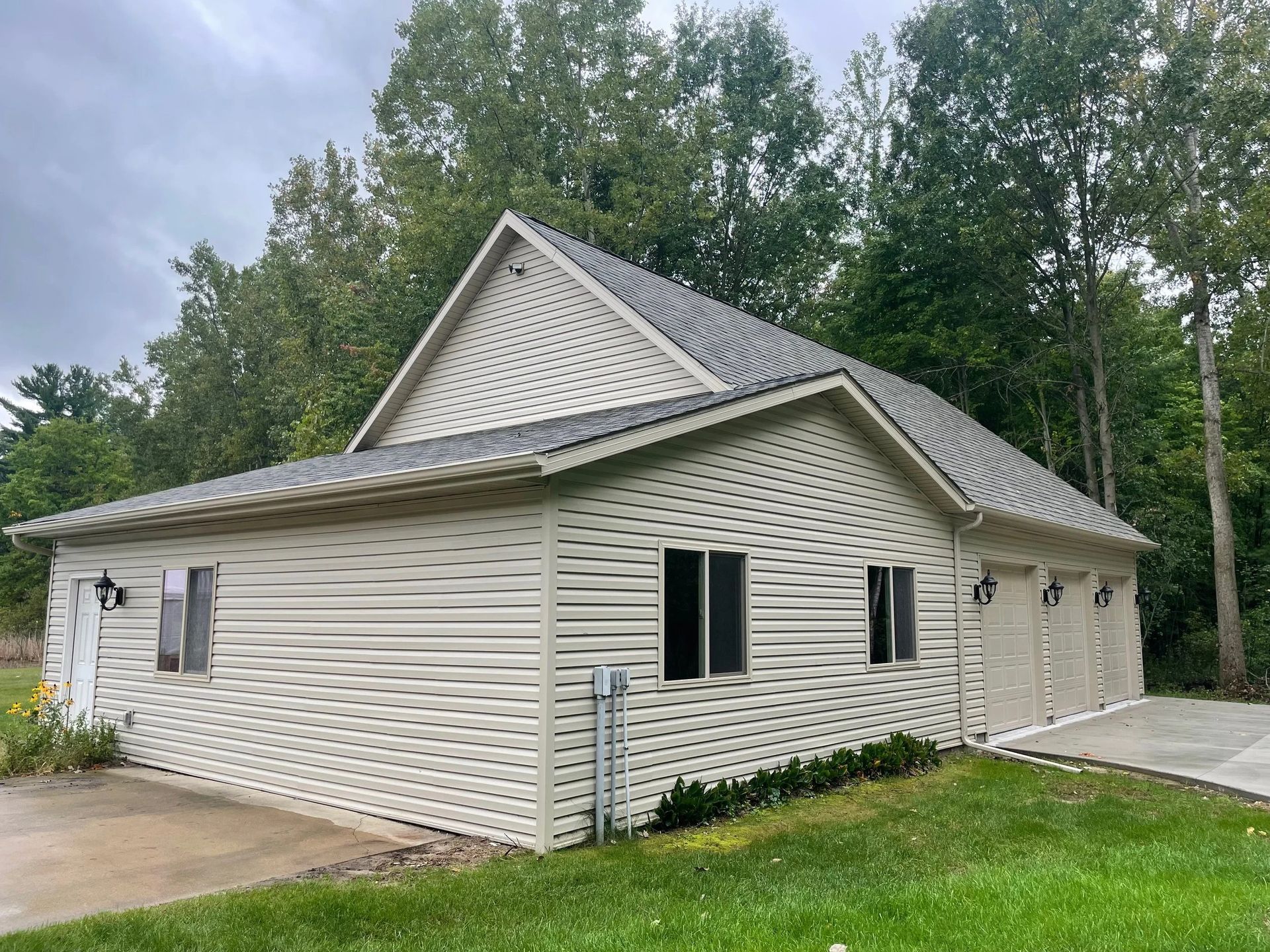 White siding house with green shutters, attached garage, and trees in the background