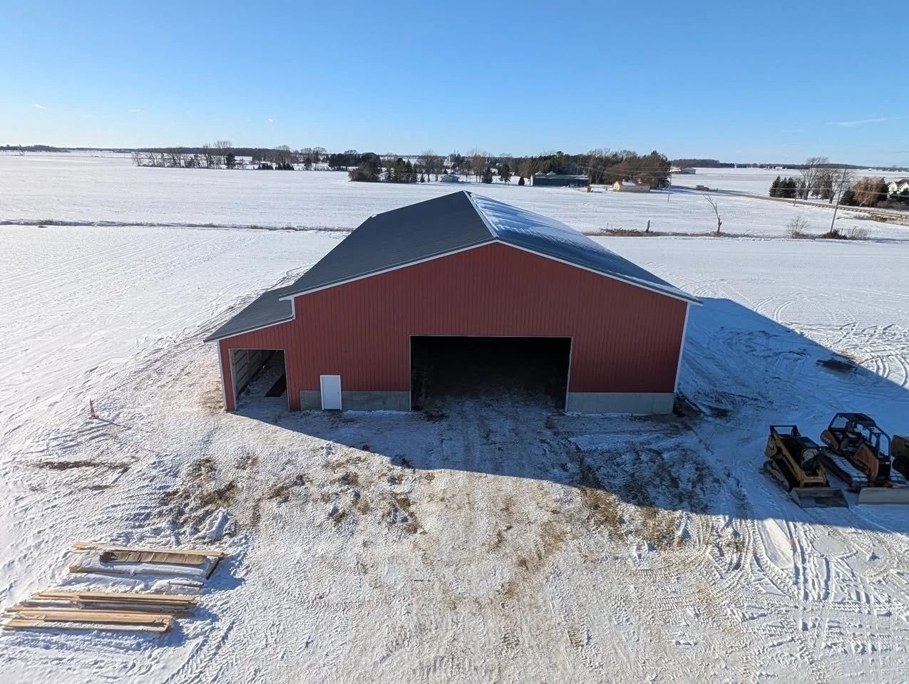 Red barn in a snowy field with farm equipment nearby under a clear winter sky