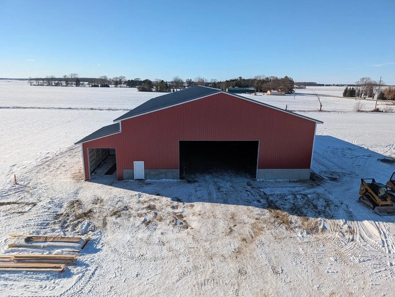 Red barn with open doorway in a snowy field under a clear blue sky
