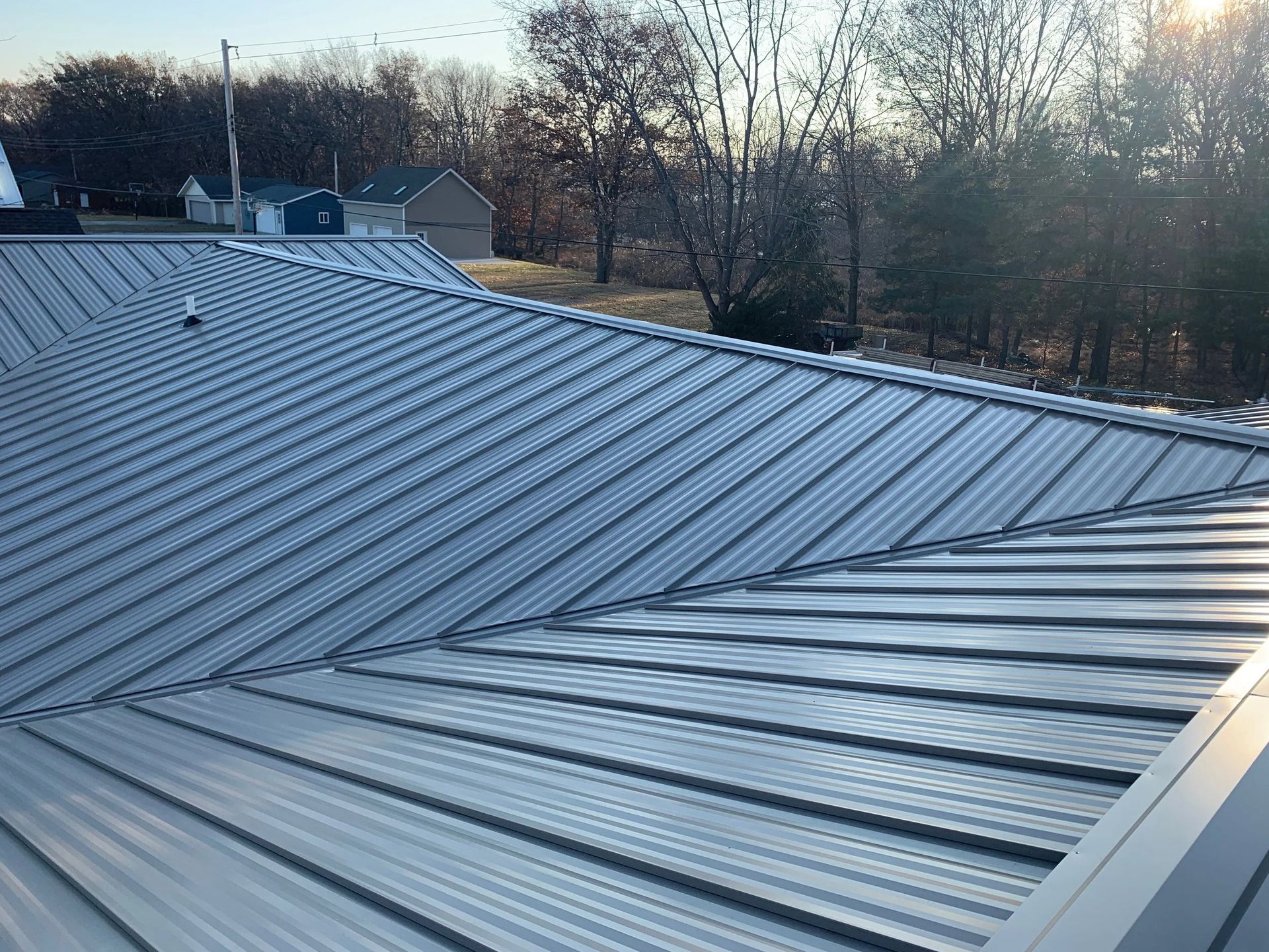 Metal roof with skylights in a wooded residential area at sunset