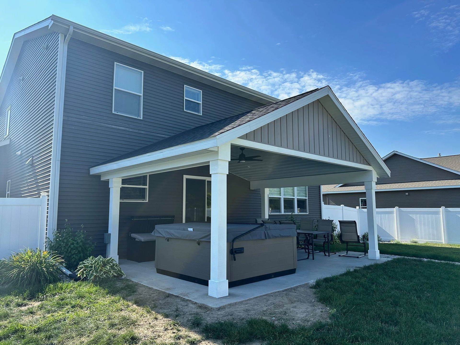Backyard patio gazebo attached to a two-story house, with white posts and a hot tub underneath