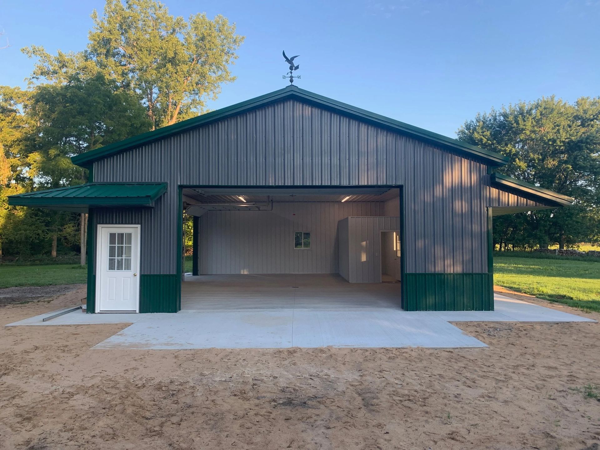 Metal barn-style garage with open double doors, green trim, and a white side door on a dirt driveway.