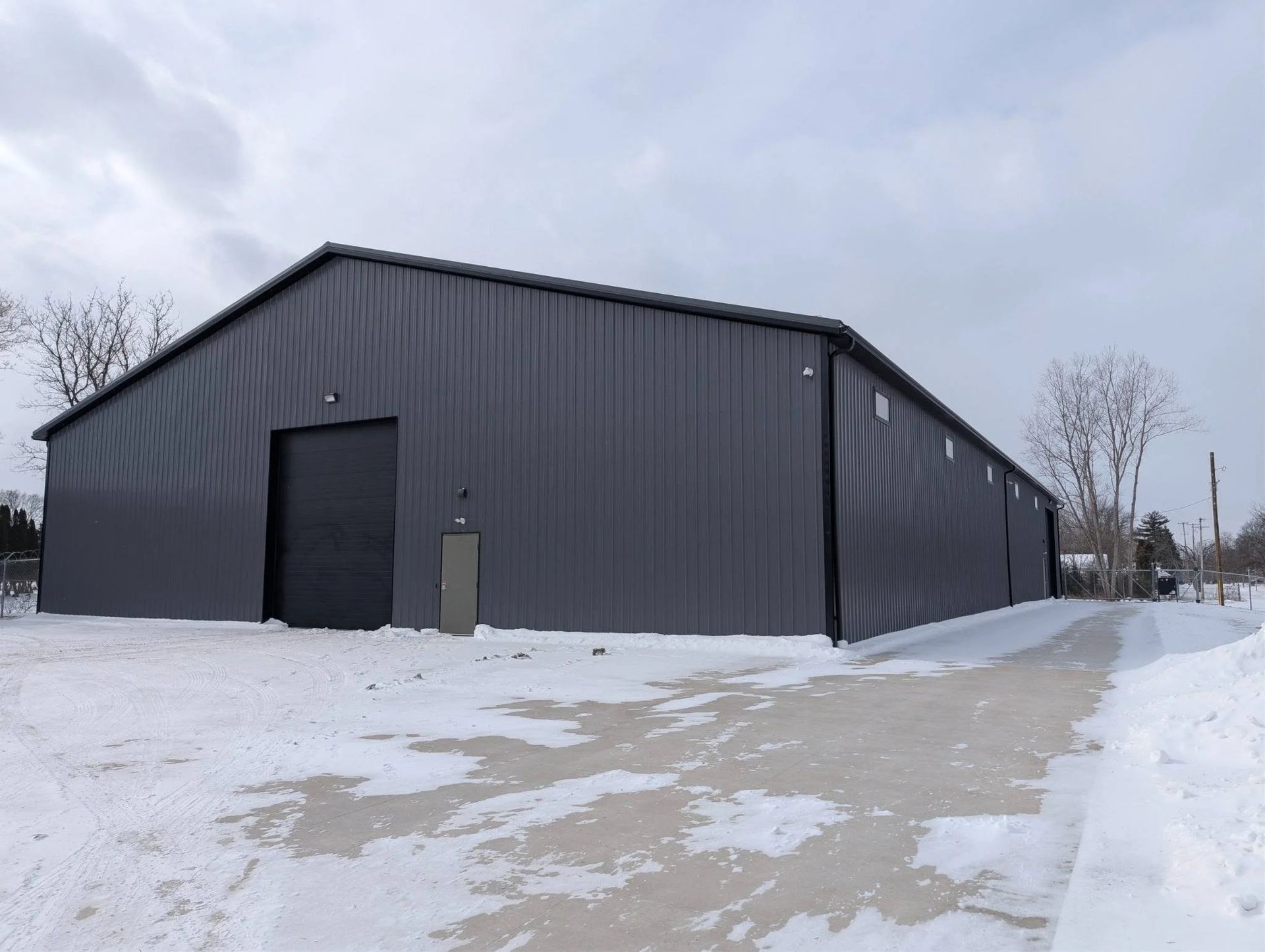 Dark gray metal warehouse beside a snowy lot under an overcast sky