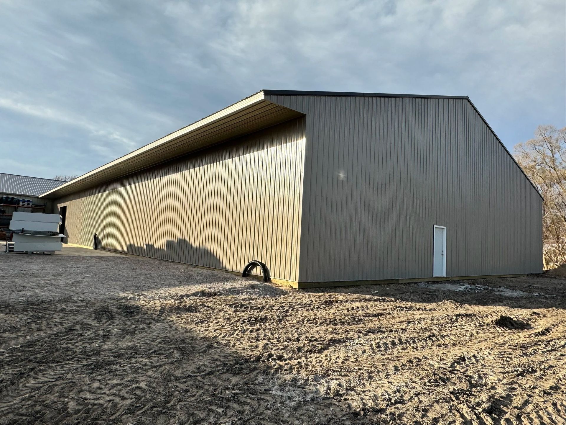 Large beige metal barn with striped wall pattern on a dirt lot under a blue sky