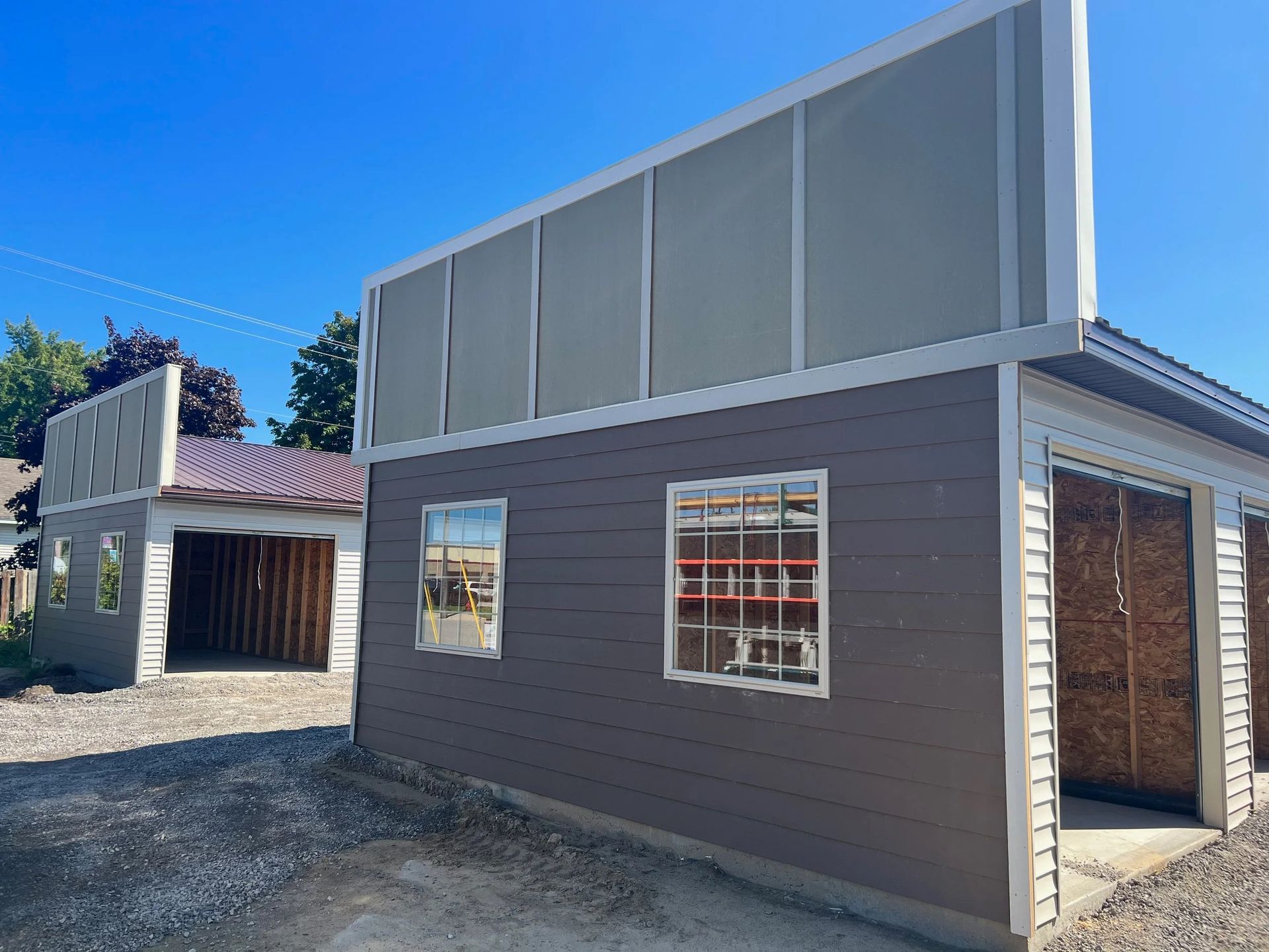 Two modern gray buildings with large windows and corrugated metal siding on a gravel lot under a blue sky
