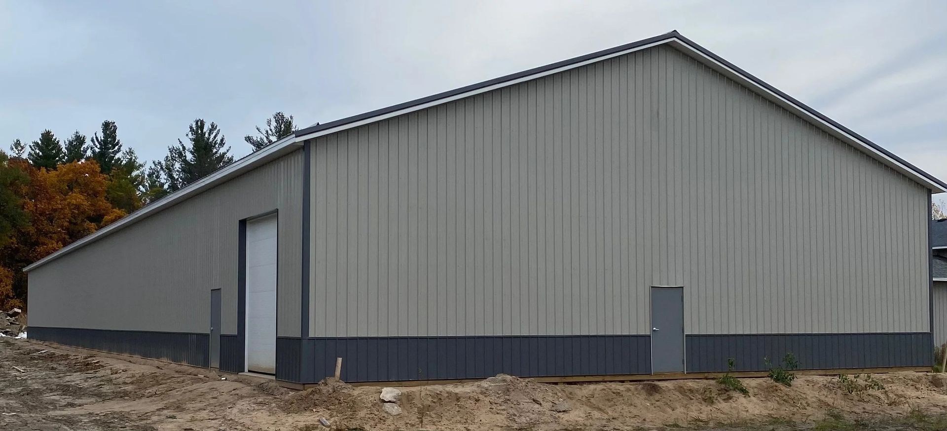 Large gray metal warehouse with a peaked roof on a gravel lot, seen from the side