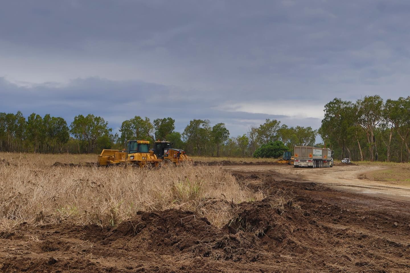 A Couple of Tractors Are Driving Down a Dirt Road in a Field — Advanced Civil Earthworks In Koah, QLD