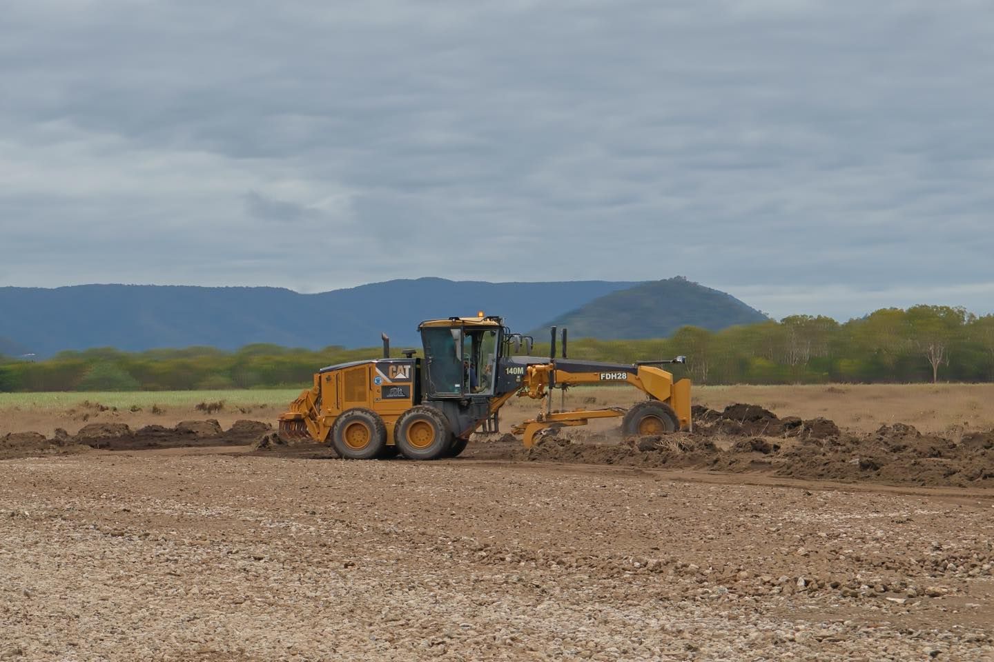 A Yellow Tractor is Plowing a Dirt Field With Mountains in the Background — Advanced Civil Earthworks In Koah, QLD