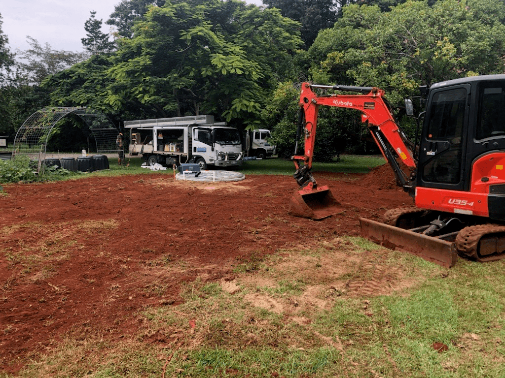 An Excavator is Digging a Hole in a Field — Advanced Civil Earthworks In Mossman, QLD