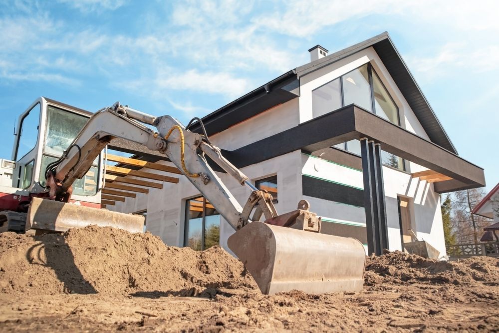 An Excavator is Digging a Hole in Front of a House Under Construction — Advanced Civil Earthworks In Mossman, QLD