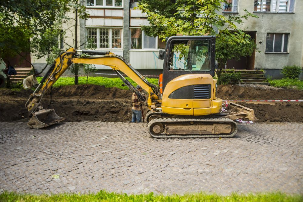 A Yellow Excavator is Digging a Hole in the Ground in Front of a Building — Advanced Civil Earthworks In Cassowary Coast, QLD