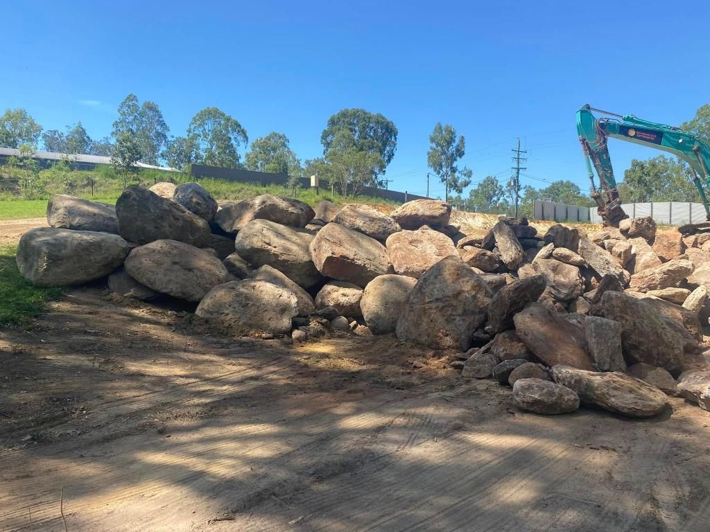 A Pile of Rocks Sitting on Top of a Dirt Road Next to a Green Excavator — Advanced Civil Earthworks In Cape York, QLD