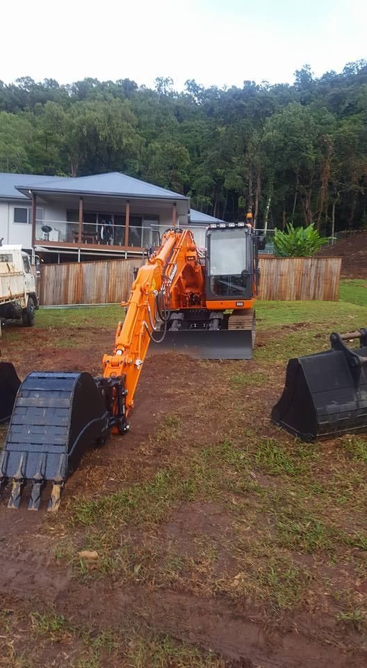 A Large Orange Excavator is Parked in a Grassy Field in Front of a House — Advanced Civil Earthworks In Port Douglas, QLD