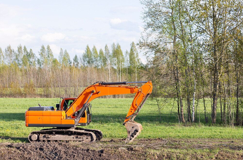 An Orange Excavator is Digging a Hole in a Field — Advanced Civil Earthworks In Townsville, QLD