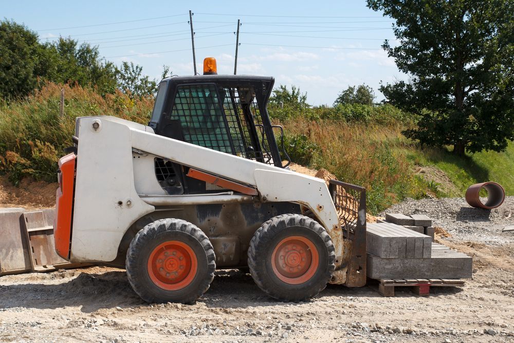 A White and Orange Skid Steer is Parked in a Dirt Field — Advanced Civil Earthworks In Tablelands, QLD