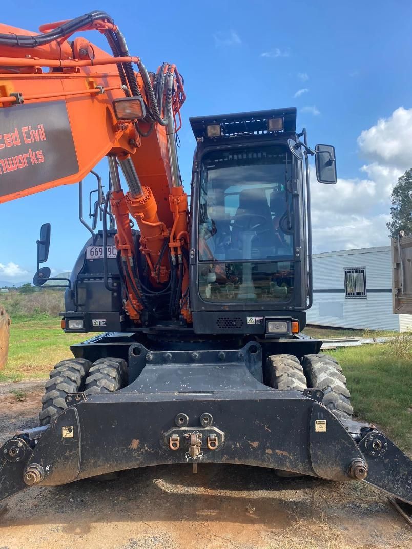 A Large Orange Excavator is Parked in a Dirt Field — Advanced Civil Earthworks In Townsville, QLD