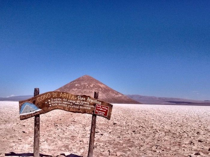 A sign in the middle of a desert with a mountain in the background