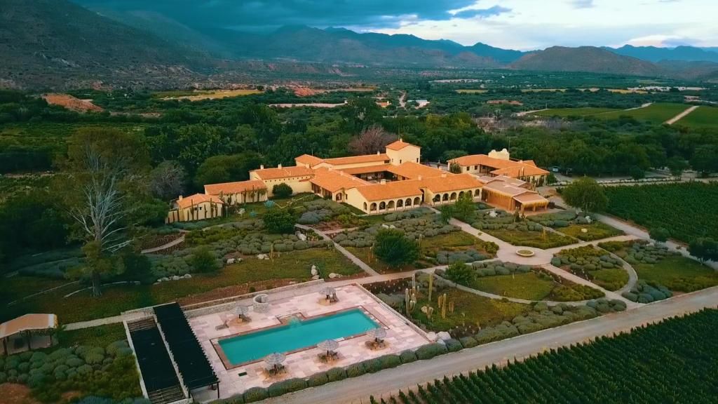 An aerial view of a large house with a swimming pool in the middle of a lush green field.
