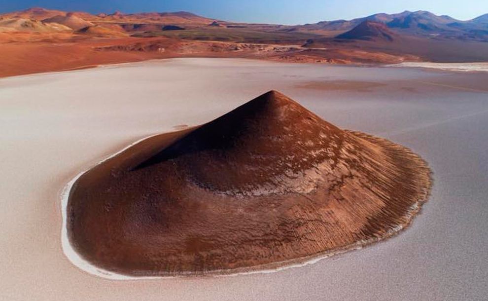 A cone in the middle of a desert with mountains in the background