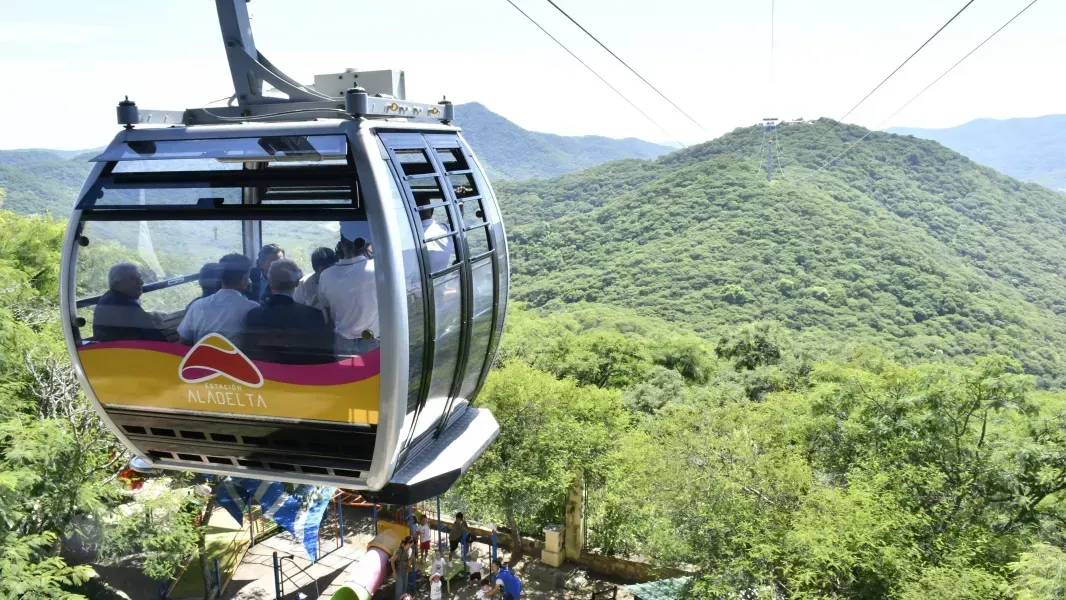 A cable car is going up a mountain surrounded by trees.