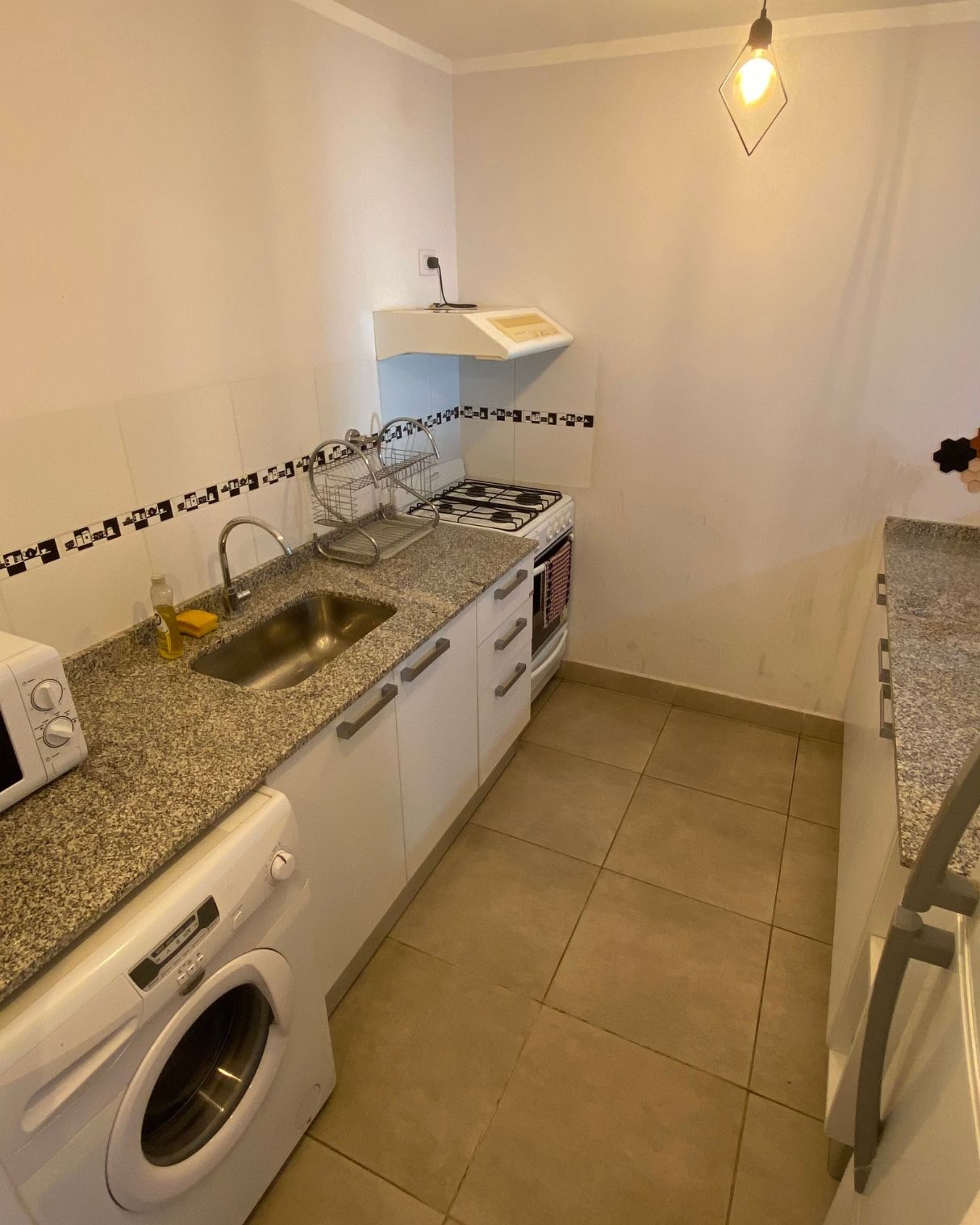A kitchen with a sink , washing machine , stove and microwave